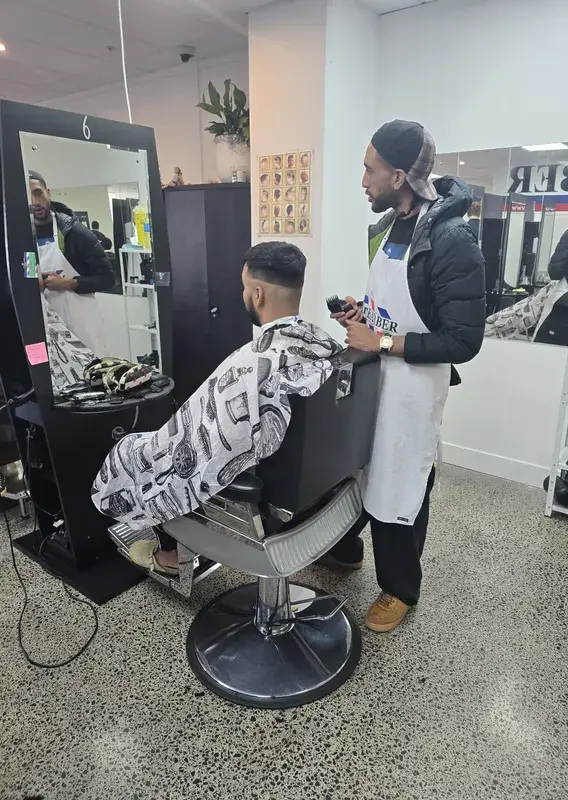 Barber running his fingers through a seated client's hair while a colleague looks on