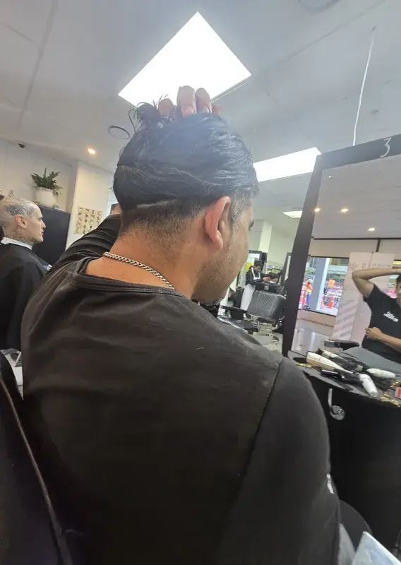 Trainee barbers in white coats walking through a busy training floor