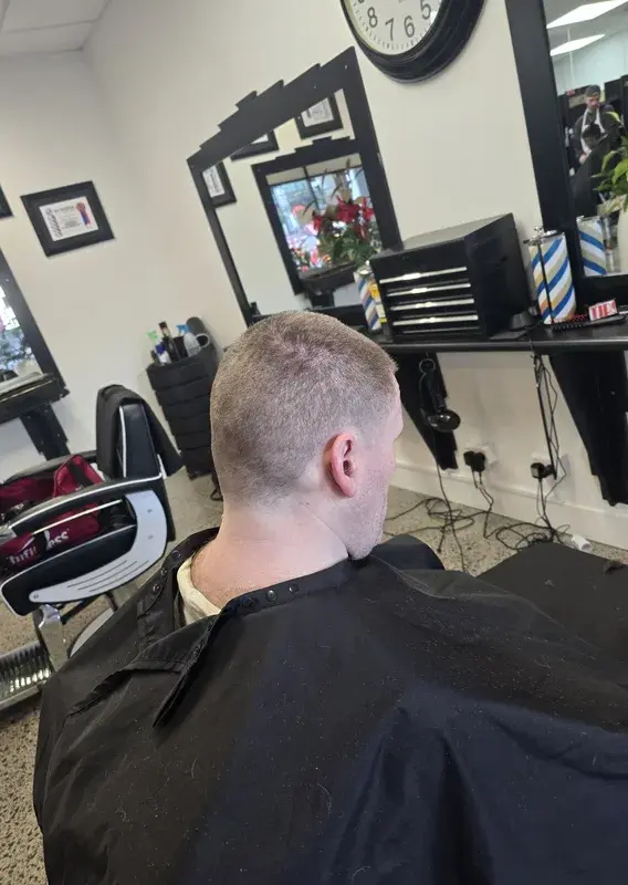 Busy barbering floor with trainees cutting hair at multiple red chairs and a barber pole